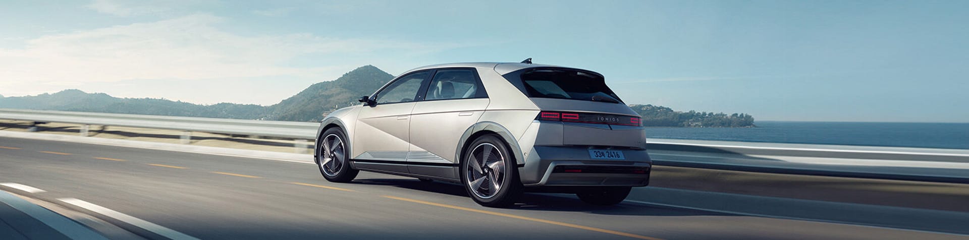 A Hyundai IONIQ 5 drives along a coastal road on a sunny day