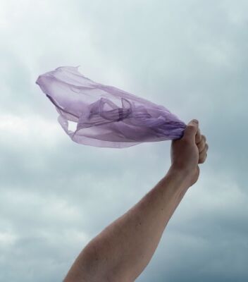 바람이 부는 가운데 한 사람이 비닐봉지를 들고 서 있습니다. 뒤로 회색빛 하늘이 보입니다. 
