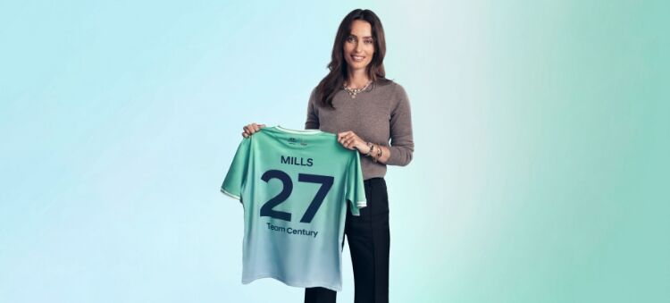Ella Mills, the award-winning cookery author, entrepreneur, and champion of plant-based living, is holding her green and blue Team Century shirt where the number 27 is written on it.