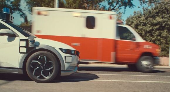 Hyundai’s IONIQ 5-based Robotaxi driving along a busy road in LA with a red and white ambulance next to it. 