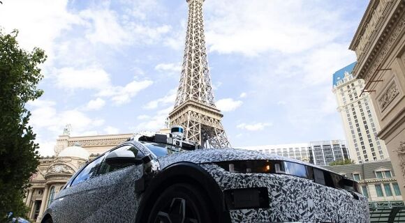 A side view of a black and white Hyundai’s IONIQ 5-based robotaxi driving past a hotel in Las Vegas.