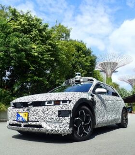 A black and while Hyundai IONIQ 5-based robotaxi driving along a road in Singapore.