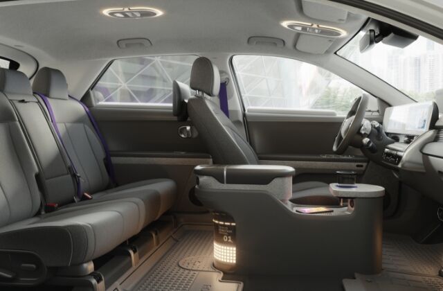 The spacious interior inside a Hyundai’s IONIQ 5-based robotaxi. There are 2 rear seats and one front seat with purple seatbelts facing a steering wheel and dashboard.