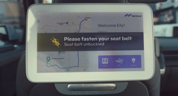 A screen on the back of the front seat in the back of a Hyundai IONIQ 5-based robotaxi that says ‘Please fasten your seatbelt, Seatbelt unbuckled’. 