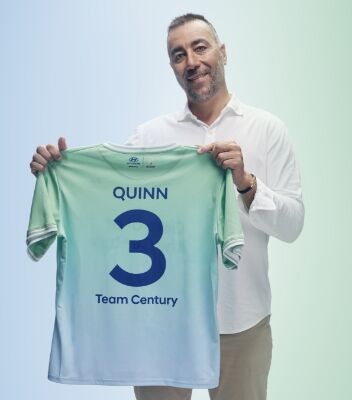 로렌초 퀸이 짙은 파란색 글씨로 “Quinn”, “3”, “Team Century”라고 적힌 녹색 및 하늘색의 팀 센츄리 유니폼을 들고 있습니다. 